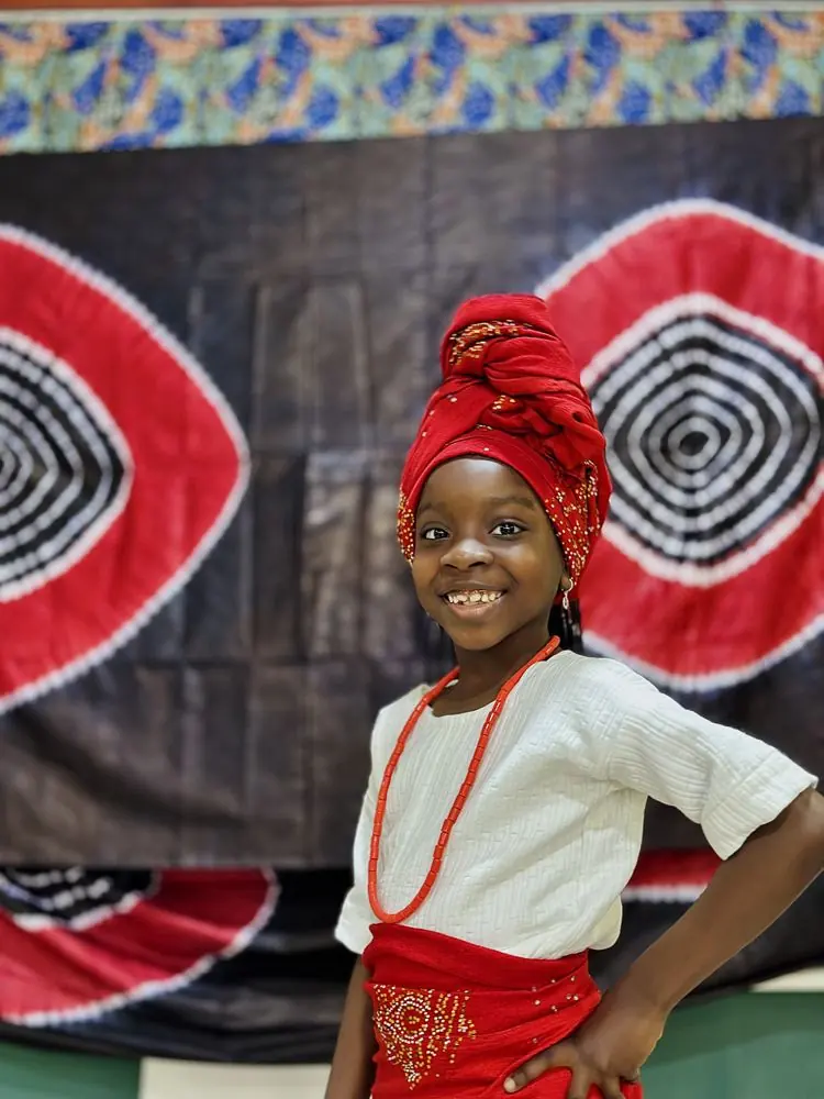 A smiling girl in a traditional red headwrap and beads