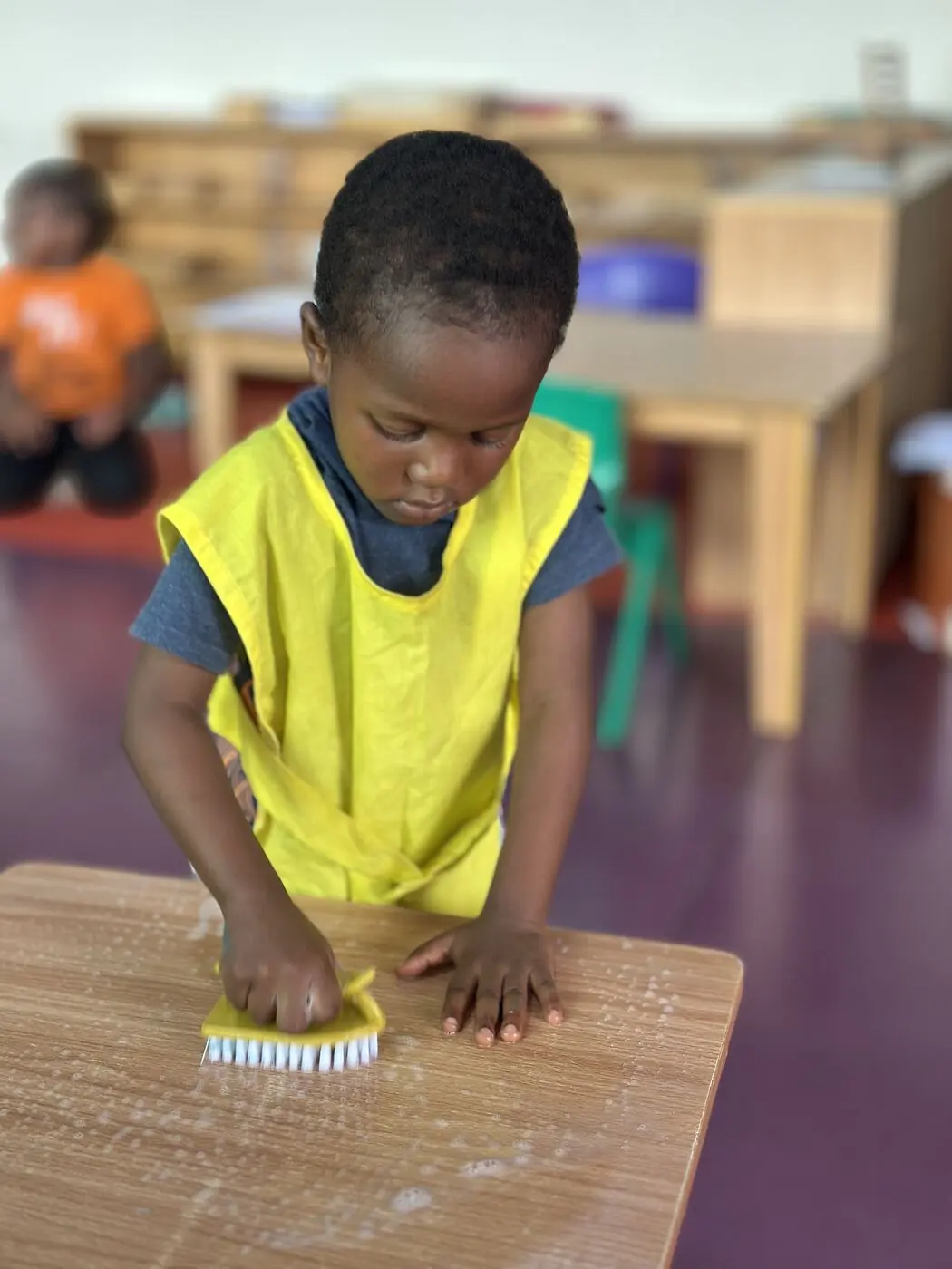 A Toddler child scrubbing a table during practical life work