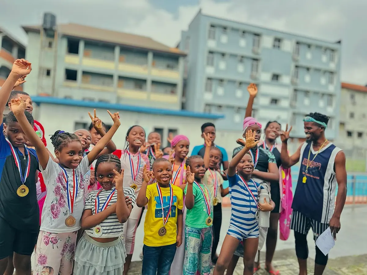 Children celebrating with medals beside a pool, with their coach